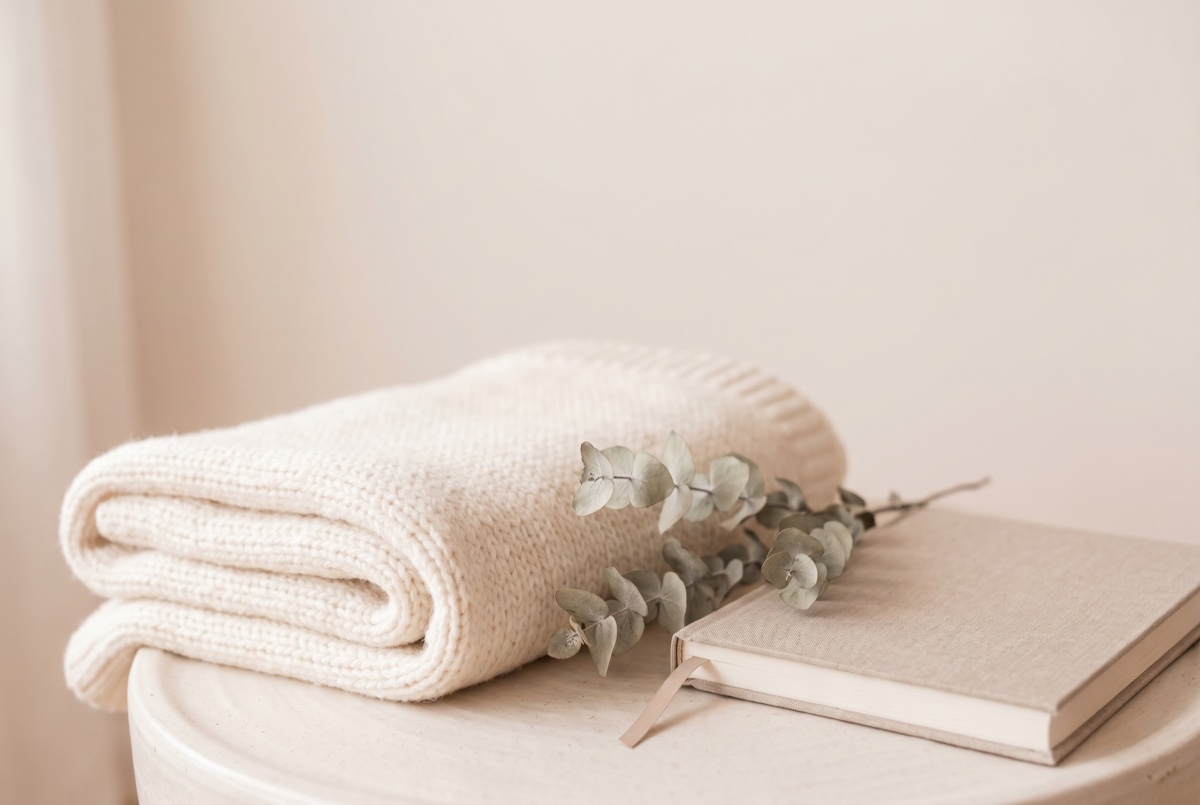 A soft blanket, dried eucalyptus, and a journal on a pale surface, evoking tender, unhurried grief and loss therapy at Anchor & Bloom