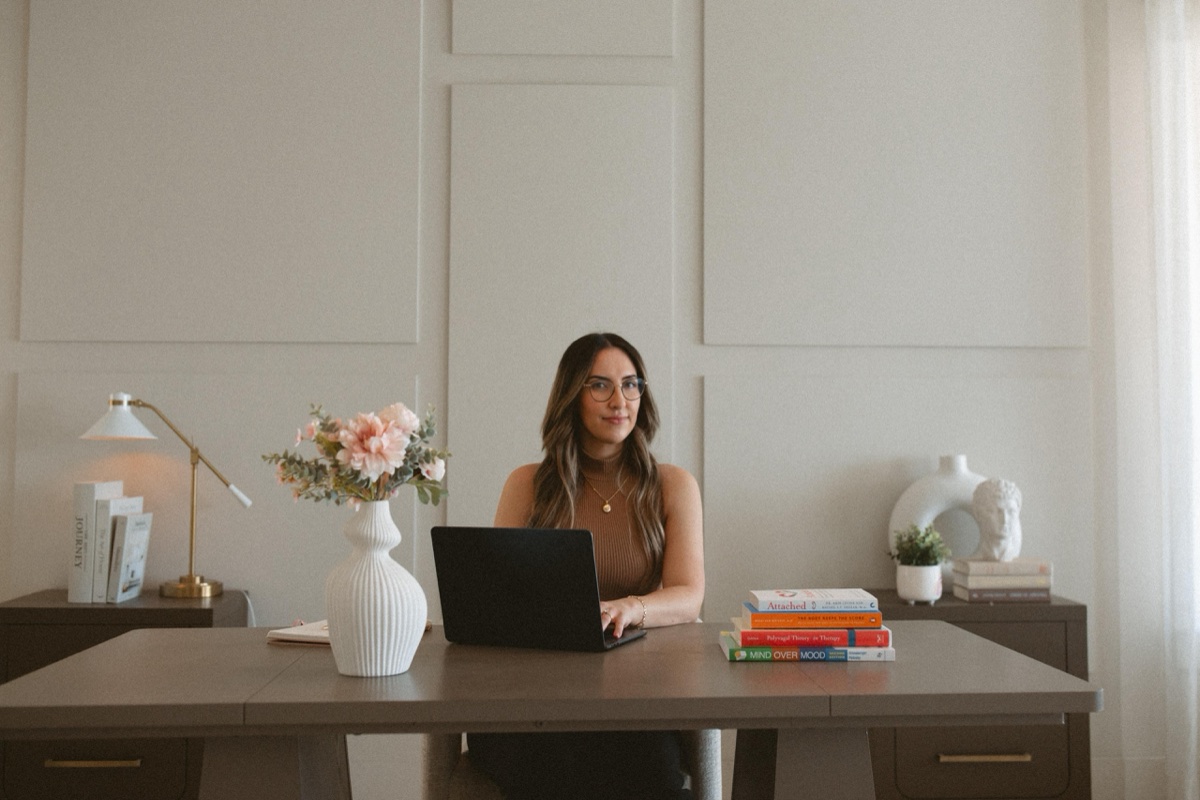 Wide view of Katelyn Matias at her desk in the Mississauga therapy office with flowers and therapy reference texts