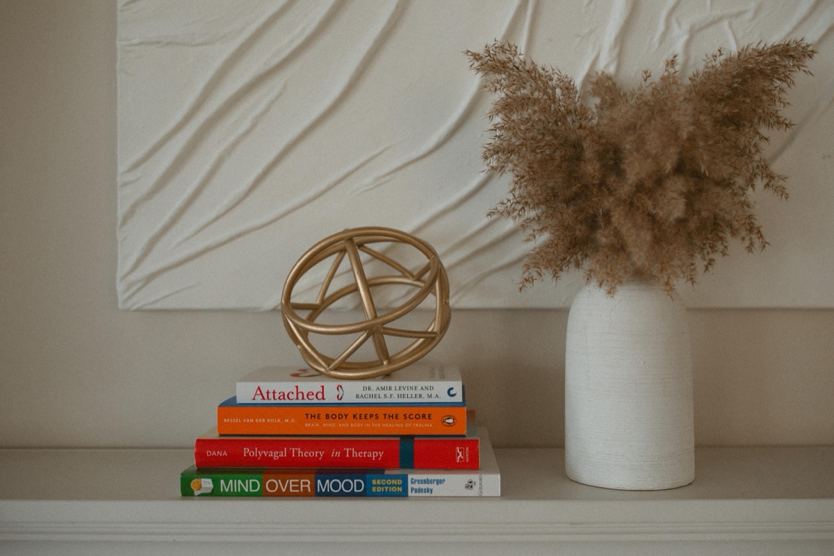 A stack of therapy books and dried pampas in a vase, evoking calm recovery from stress and burnout at Anchor & Bloom