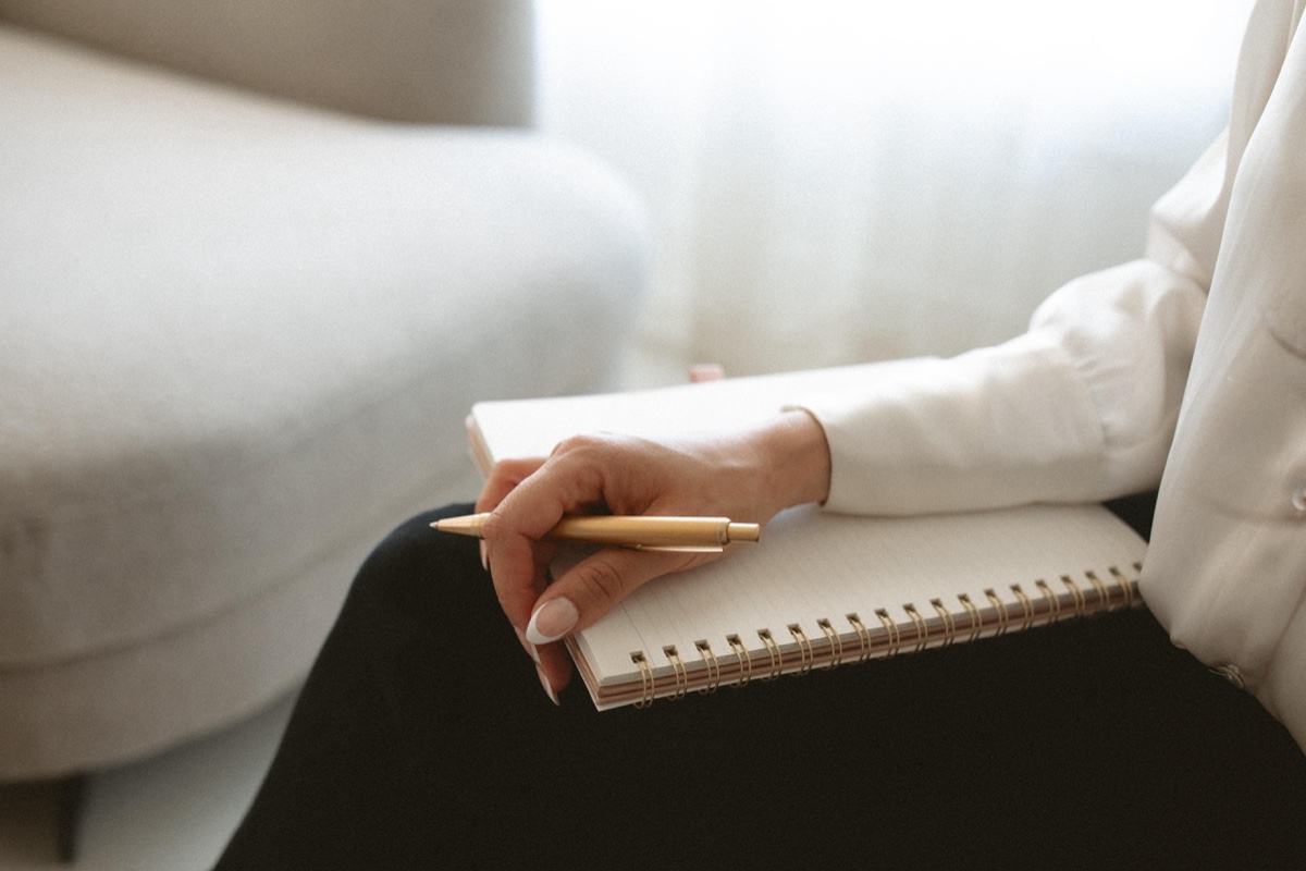 A hand resting with a gold pen on an open notebook, evoking reflective support through life transitions at Anchor & Bloom