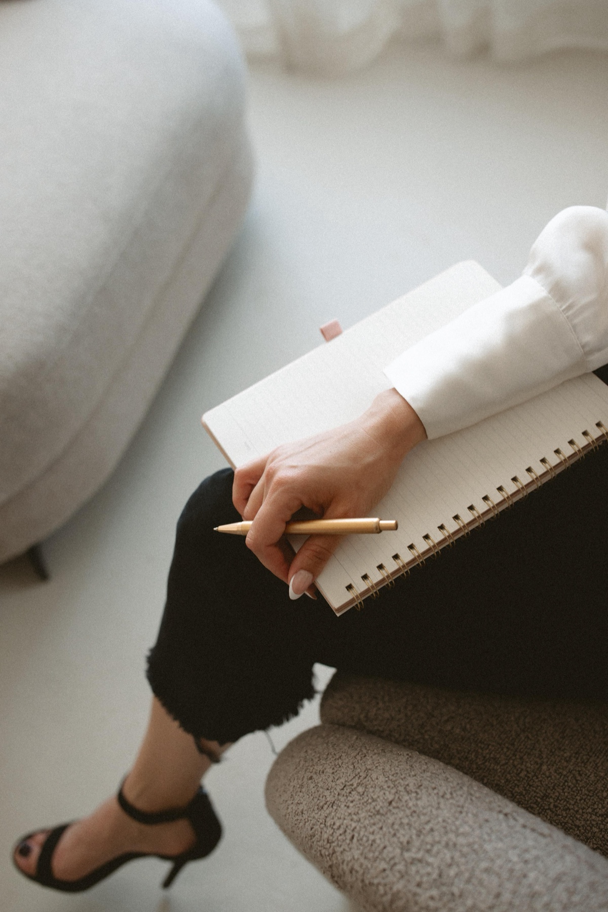 A woman journaling with a gold pen in a spiral notebook, a calm, reflective moment in the therapy space