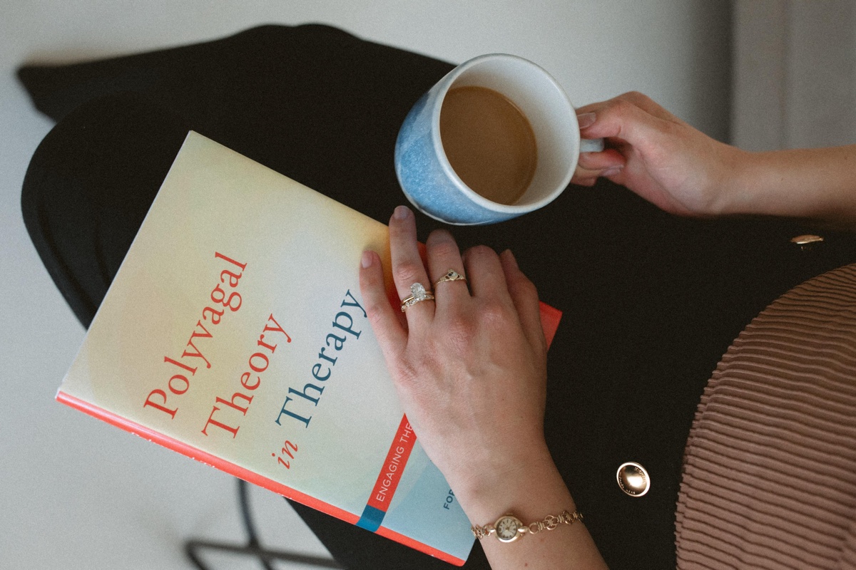 Deb Dana's Polyvagal Theory in Therapy beside a warm cup of coffee, evoking grounded nervous system regulation work at Anchor & Bloom